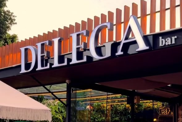 Letreiro do Delega sobre o ripado de madeira, com a varanda e o salão envidraçado