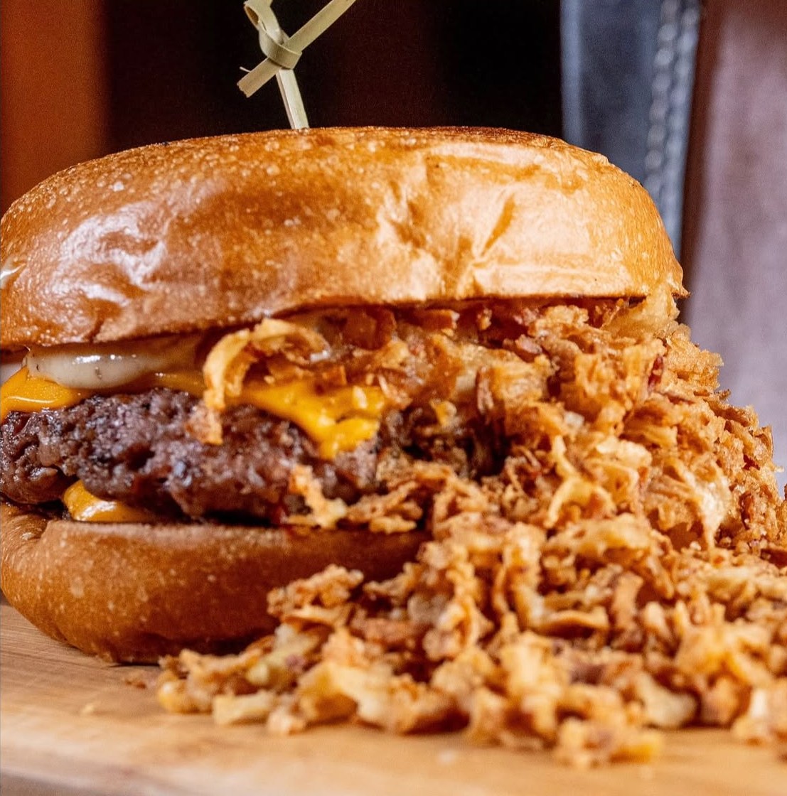 Hambúrguer com cheddar derretido e uma montanha de cebola crispy na tábua